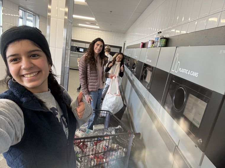 Students at a bottle-return machine with a shopping cart full of cans and bottles during the National Honor Society bottle drive
