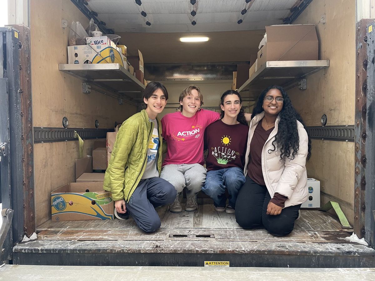 Four Crunch the Hunger students kneeling in the back of a box truck loaded with boxes of donated food